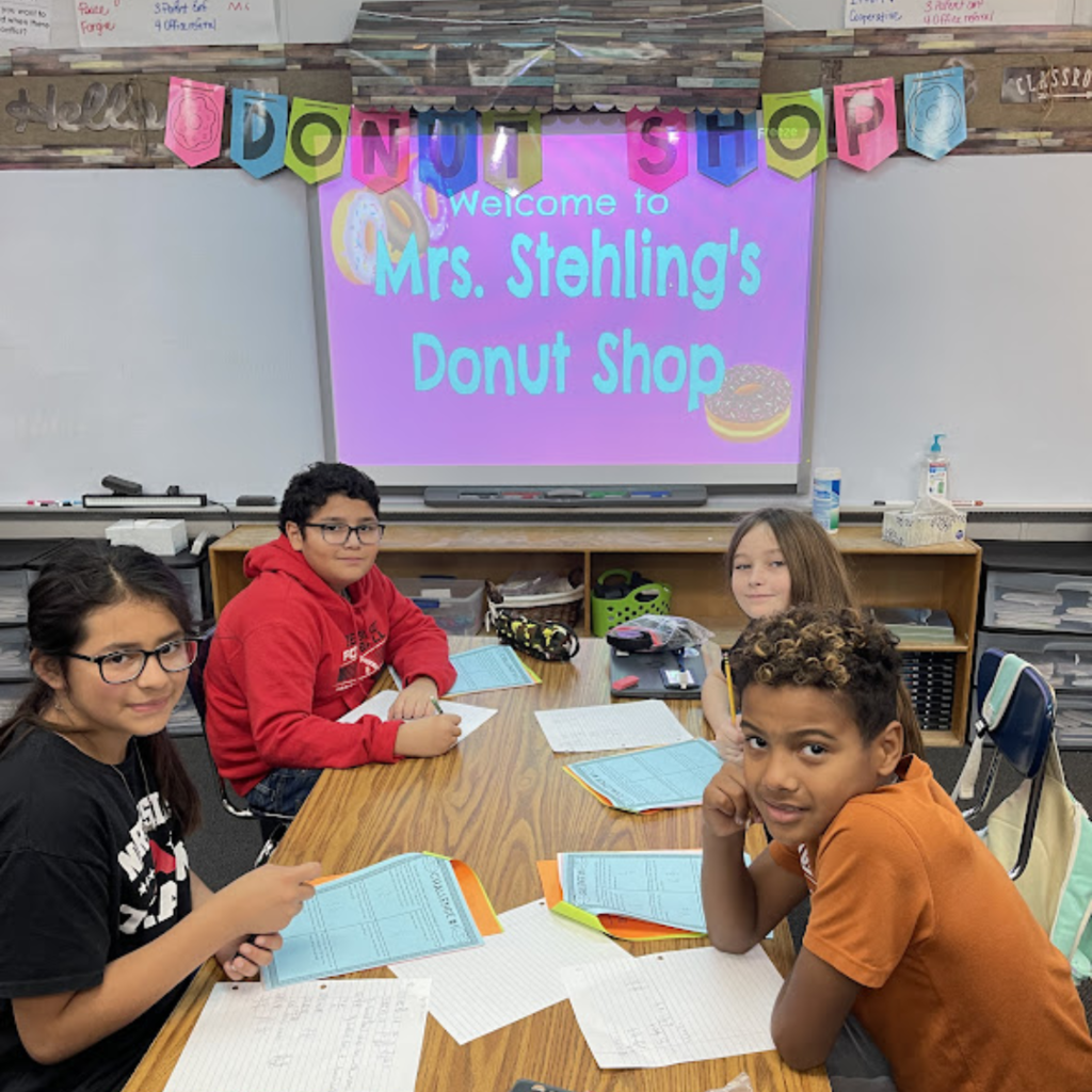 4 students at their desks with review sheet by a sign that reads mrs. stehling's donut shop