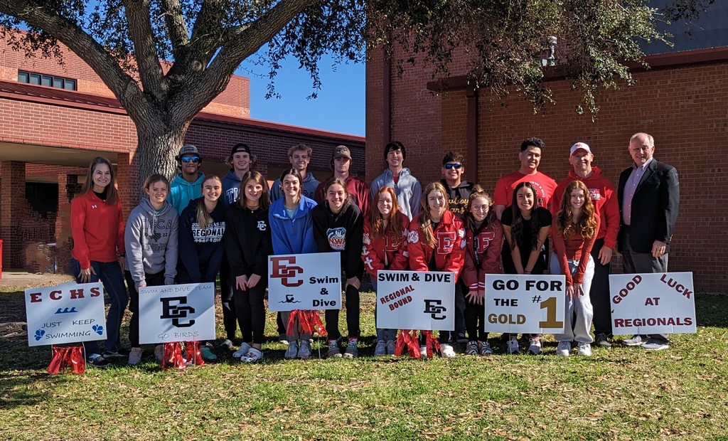 swim and dive team posing with coaches and superintendent by good luck signs